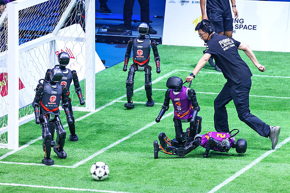 A fallen robot being helped by the referee as a teammate robot stands nearby during China’s first fully autonomous AI robot football match