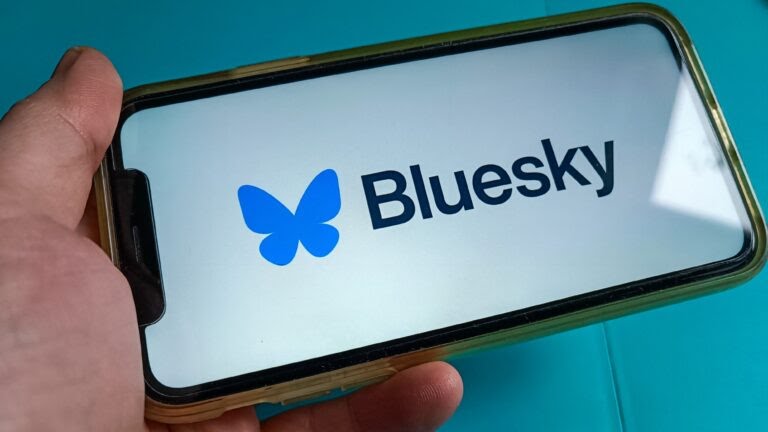 Hand holding a smartphone displaying the Bluesky logo, representing the rise of a decentralized social media platform