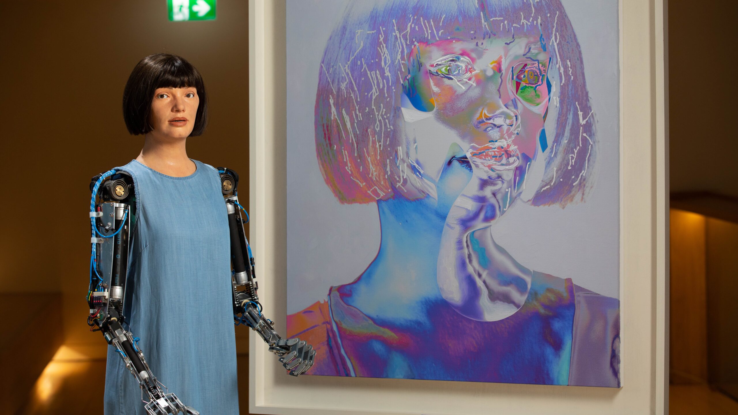 Humanoid robot artist Ai-Da interacting with a visitor while painting at an exhibition, surrounded by lights