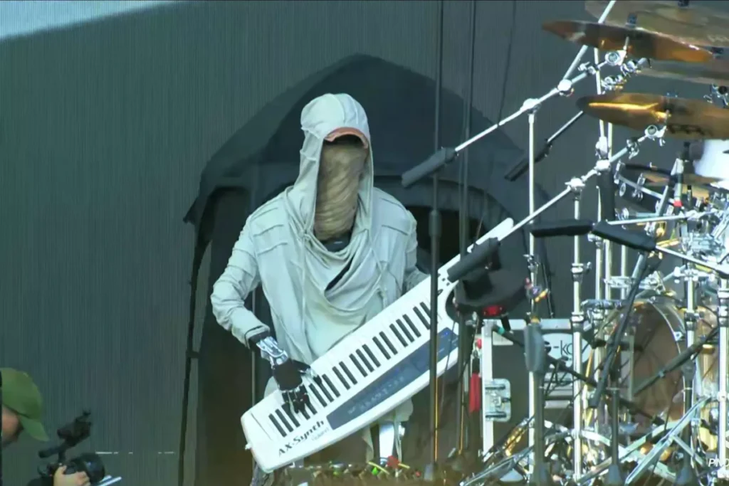 Funky humanoid robot rocks the keys during a live music festival performance, wearing a hoodie and cap.