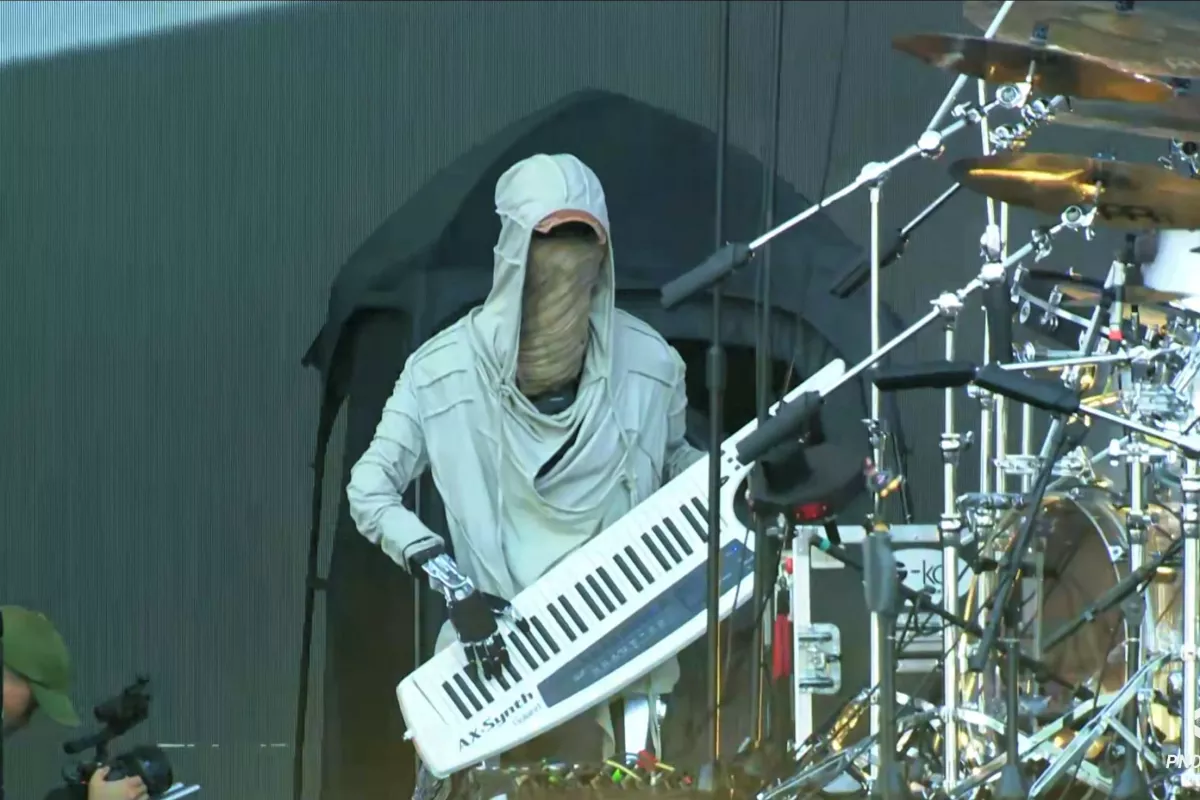 Funky humanoid robot rocks the keys during a live music festival performance, wearing a hoodie and cap.