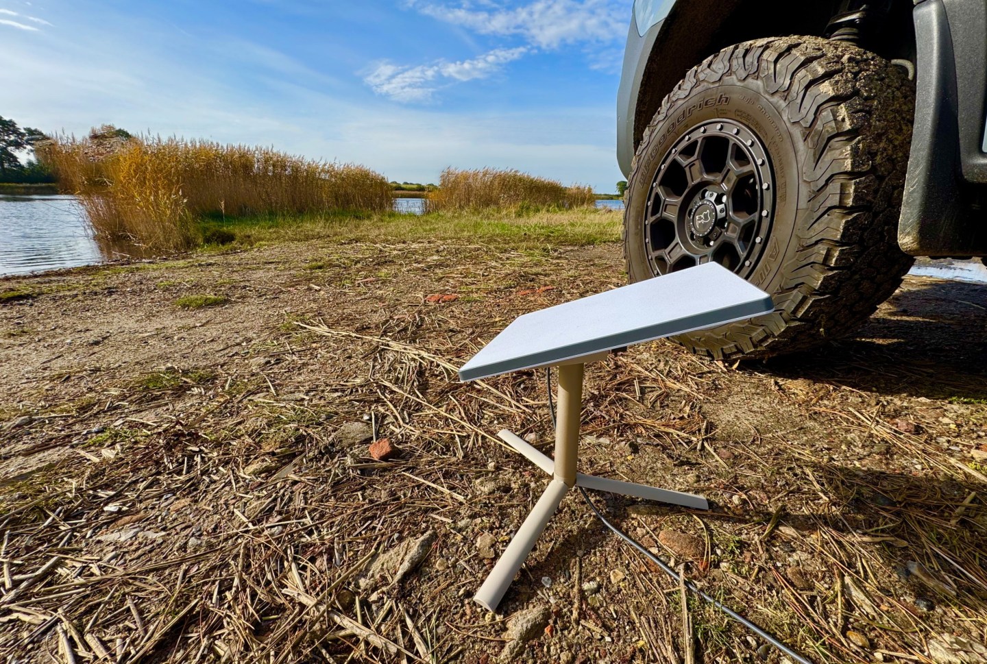 Starlink Mini satellite dish set up beside an off-road vehicle near a lake, providing portable internet connectivity.