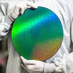 Technician holding a quantum chip wafer in cleanroom environment showcasing real-world quantum computing applications.