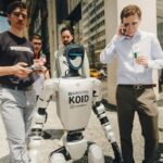 A humanoid robot strolls NYC streets, wearing sneakers and surrounded by surprised pedestrians in Midtown Manhattan.