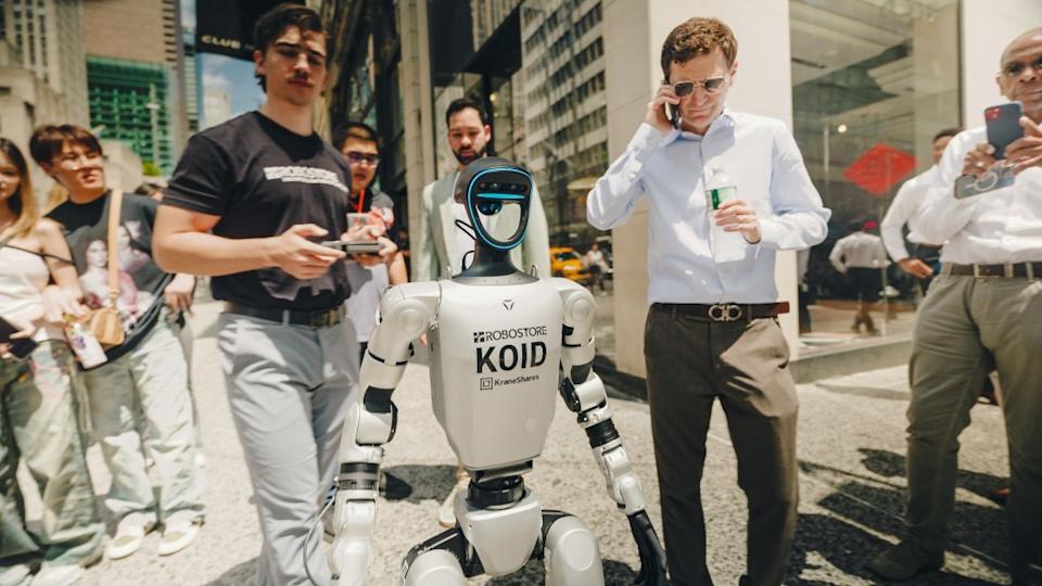 A humanoid robot strolls NYC streets, wearing sneakers and surrounded by surprised pedestrians in Midtown Manhattan.
