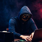 A hacker in a dark hoodie using a laptop with Google’s logo, warning signs, and a locked folder icon, symbolizing the recent security breach where Google has been hacked and user data stolen.