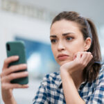 A teenage girl looking sad while holding her phone, highlighting the risks of teens hospitalized after talking to AI chatbots.