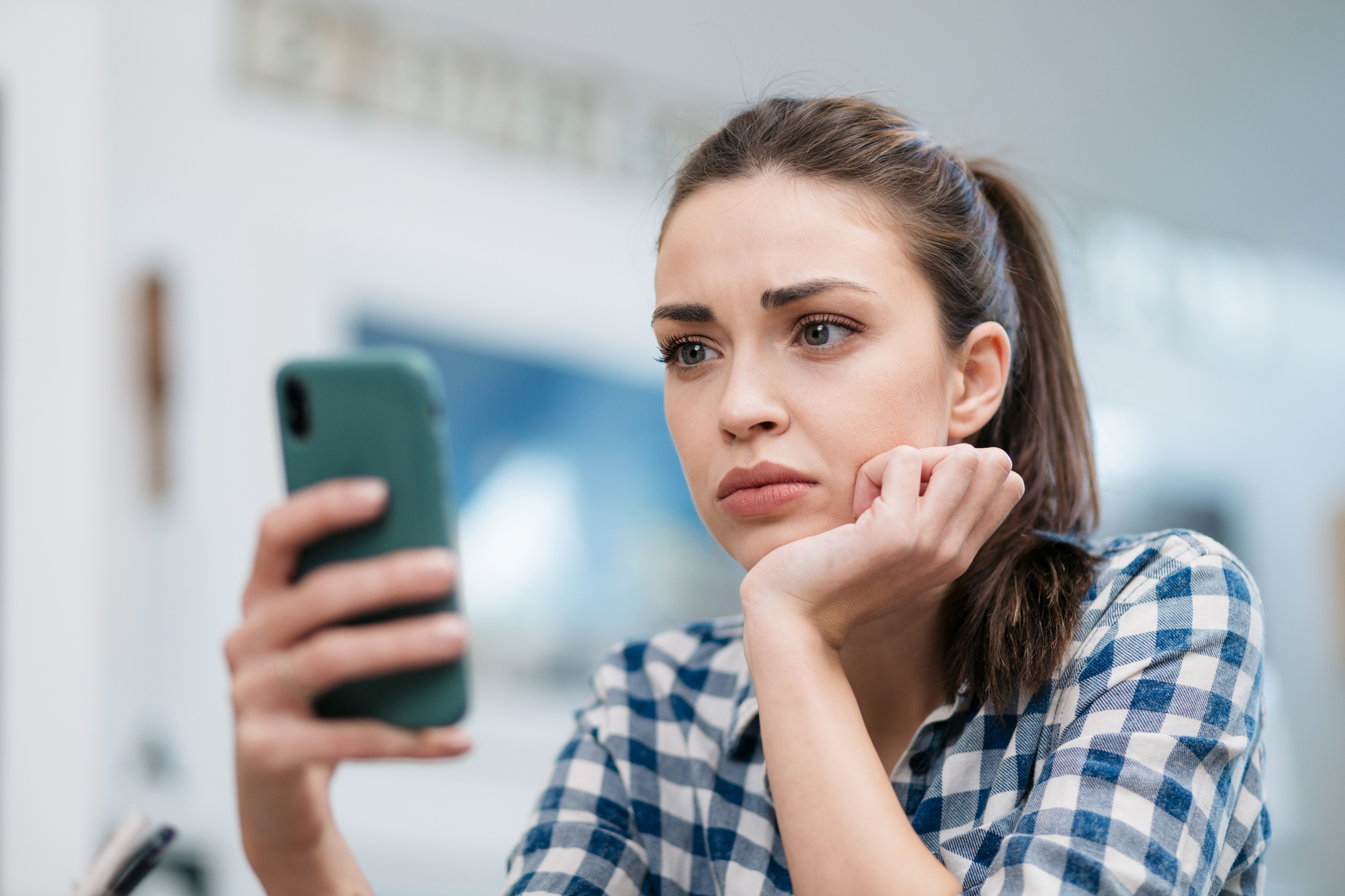 A teenage girl looking sad while holding her phone, highlighting the risks of teens hospitalized after talking to AI chatbots.
