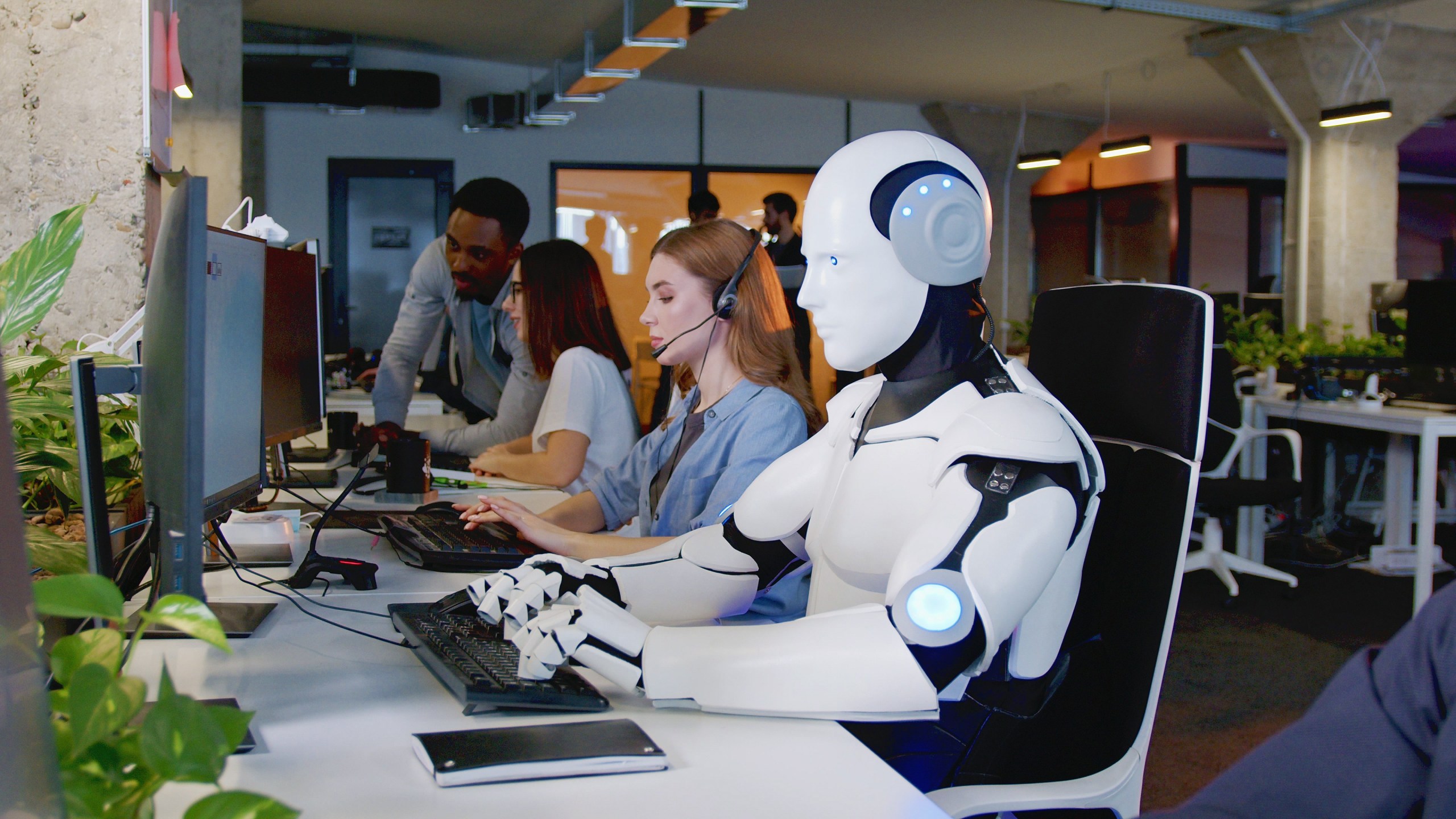 Humanoid robot working alongside human employees in a modern office, highlighting the AI job threat in customer service roles.