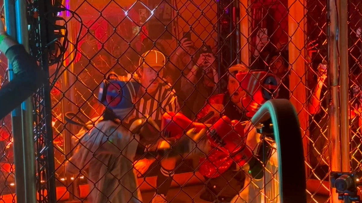 Humanoid robots battling inside a cage during a live robot fight San Francisco event with referee and cheering audience.
