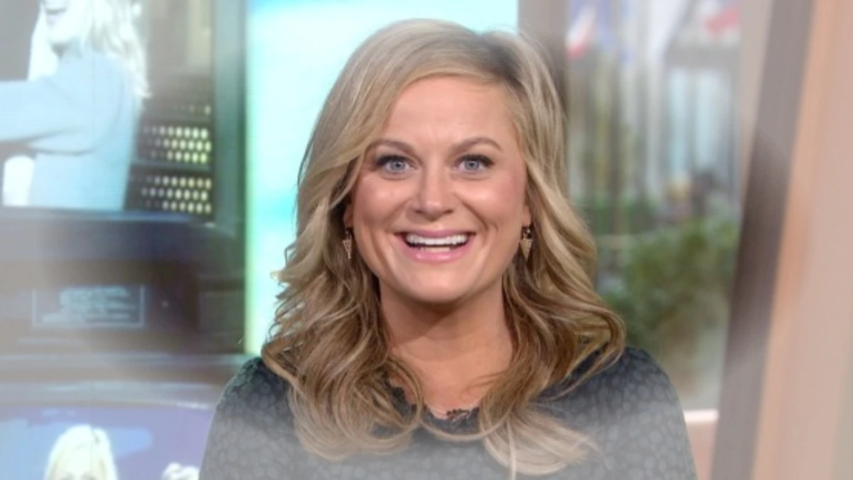 Smiling woman in a studio during a television appearance, representing Amy Poehler AI Actress discussion on SNL’s 50th anniversary