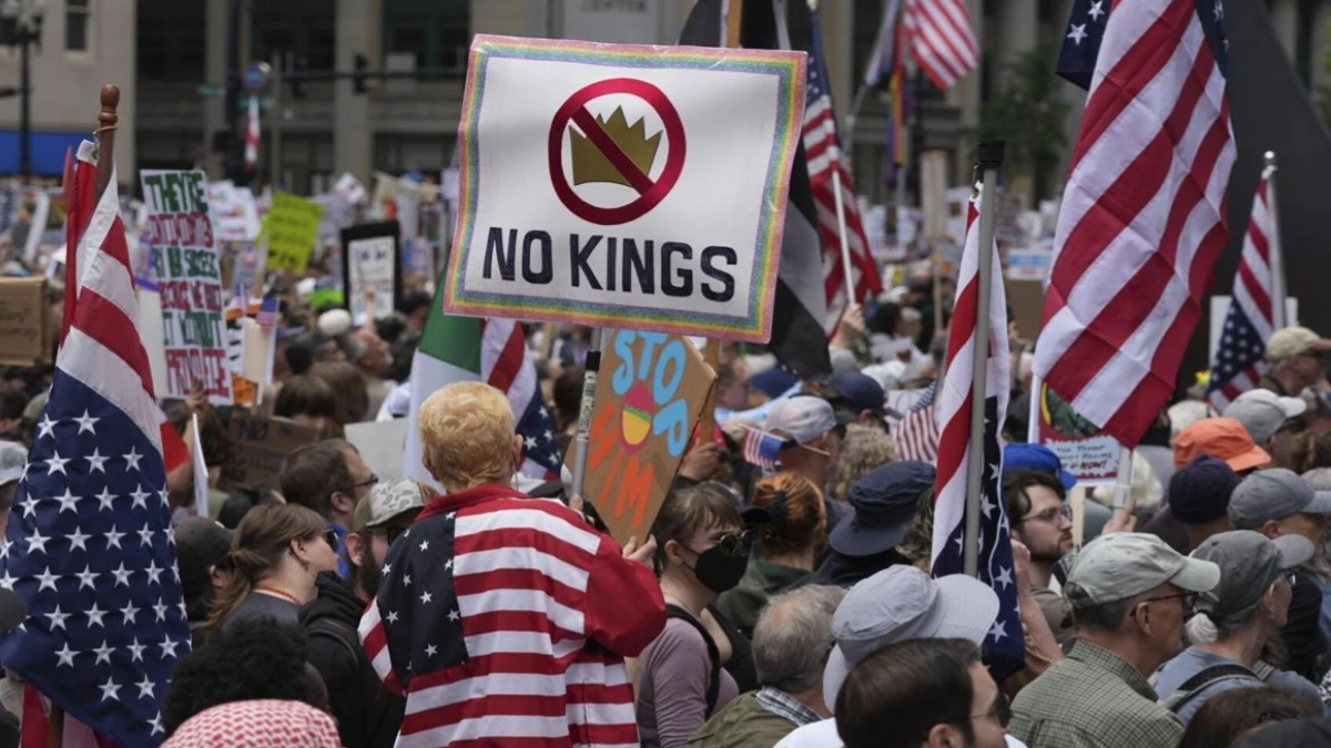 Crowds wave American flags and hold signs reading No Kings protests during nationwide anti Trump demonstrations.