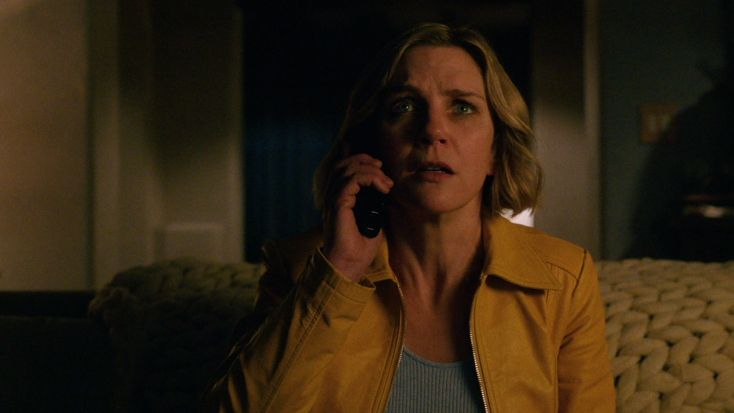 Rhea Seehorn as Carol Sturka in Vince Gilligan’s Apple TV drama Pluribus, standing pensively in a softly lit room, reflecting the show’s themes of isolation and identity.
