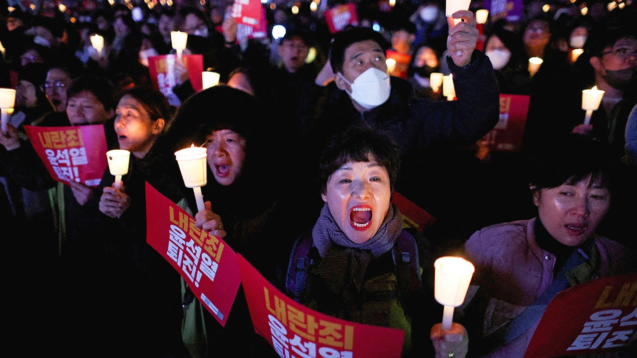 Crowds gather near South Korea’s national assembly during the anniversary of the South Korea martial law crisis, with pro-democracy groups and Yoon supporters holding flags.