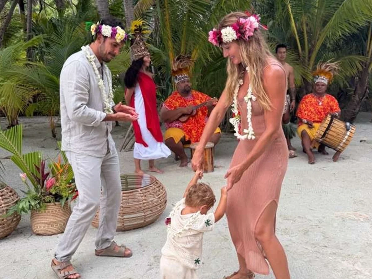 Gisele Bündchen and Joaquim Valente dance with their 1-year-old son during a cultural celebration in Tahiti as local musicians perform in the background.