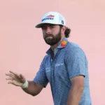 Professional golfer acknowledges the crowd during the final round of The Open Championship at Royal Birkdale while wearing a white cap and blue striped polo shirt.