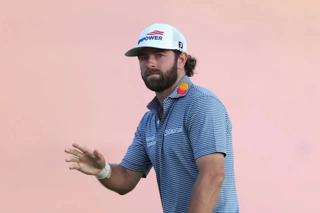 Professional golfer acknowledges the crowd during the final round of The Open Championship at Royal Birkdale while wearing a white cap and blue striped polo shirt.