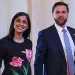 Second Lady Usha Vance and Vice President JD Vance stand together inside a government building, smiling during an official event following the announcement of the birth of their fourth child.