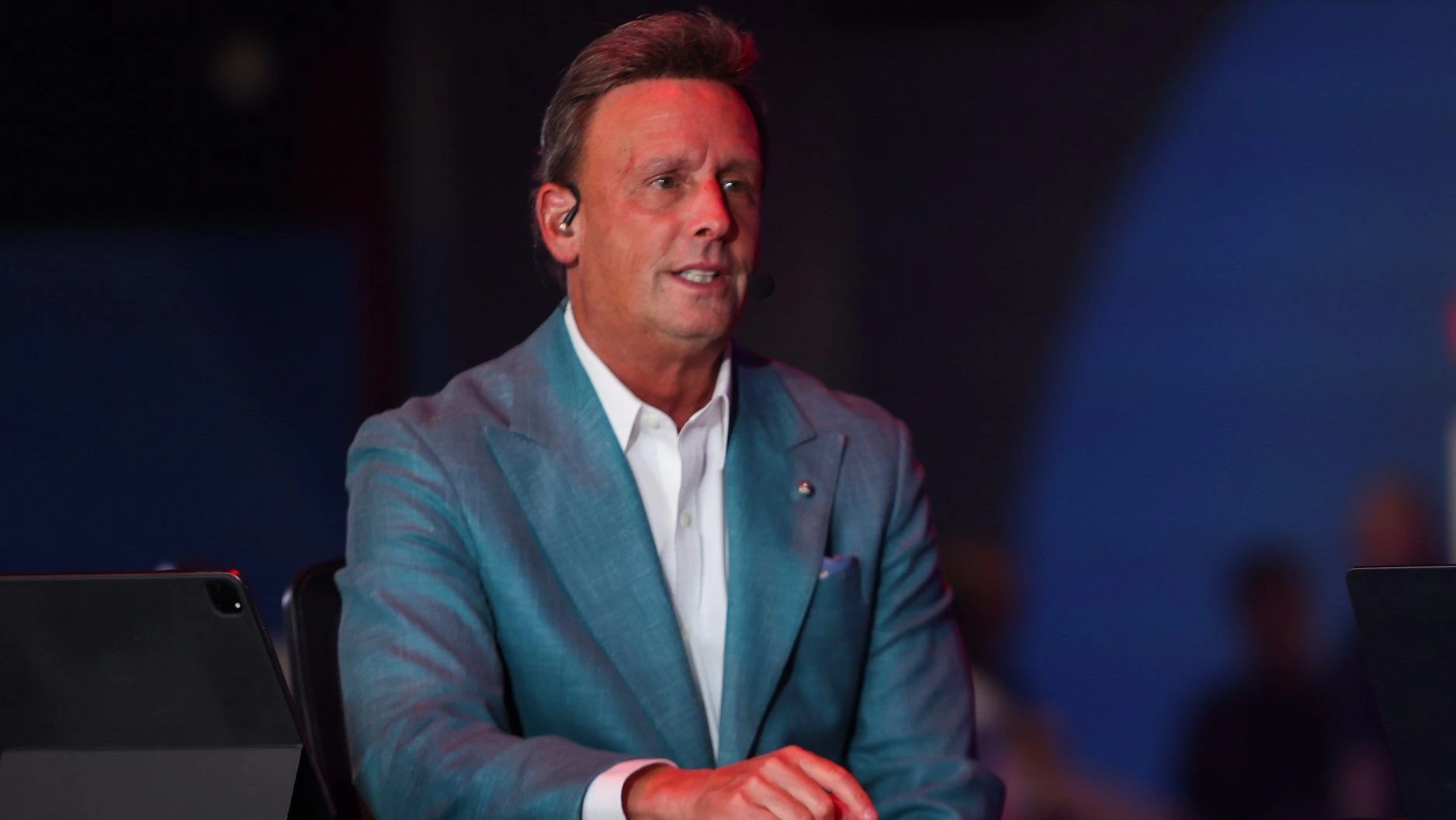 Karl Ravech appears on an ESPN broadcast set wearing a light blue blazer and headset during a live sports television production.
