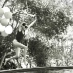 Meghan Markle jumps into a swimming pool holding birthday balloons while celebrating her 45th birthday in a black-and-white photo.